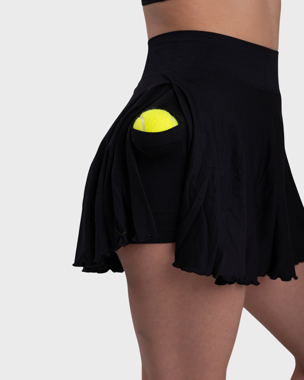 Tennis Skirt in black – close-up of the built-in shorts pocket holding a tennis ball